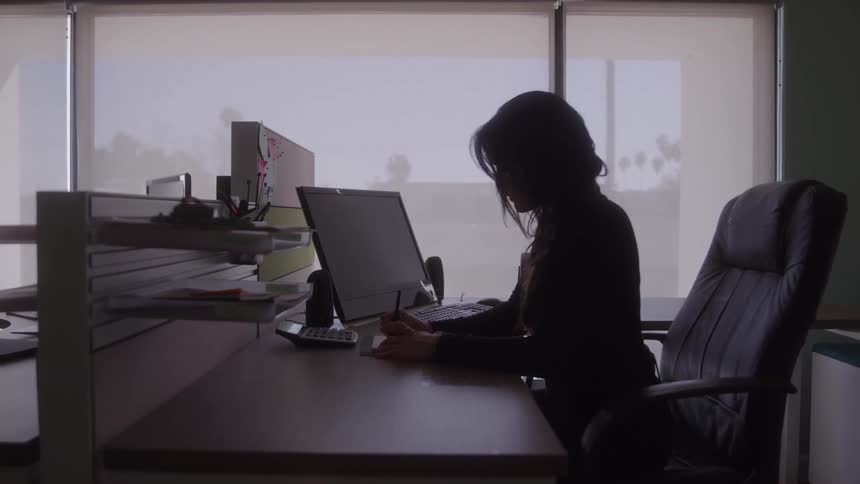 A young woman sitting in her office writing on a piece of paper and looking a bit anxious