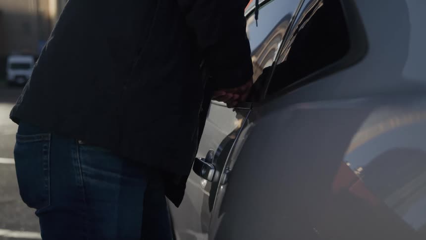 A man approaching a car breaking open the door and then getting inside the car