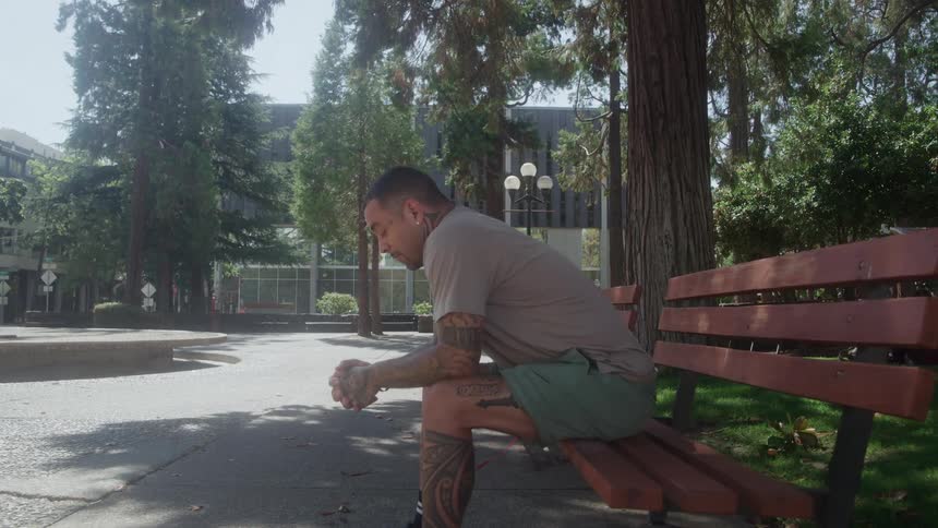 A man sitting on a bench in an outdoor park with his hands together praying