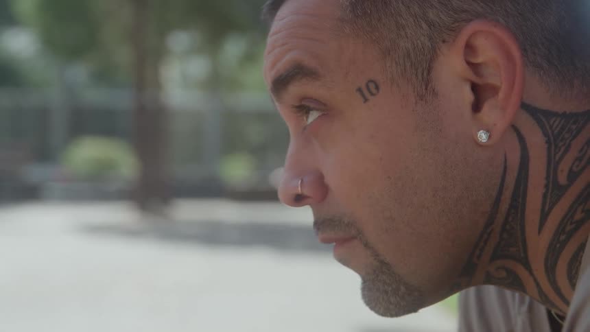Man with tattoos on his face and neck looking thoughtfully to the side