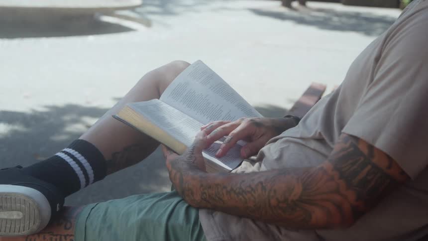 Tattooed man sitting and reading a book outdoors