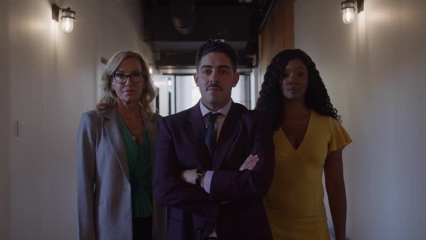Two women stand beside a man in a hallway with the middleaged woman on the left wearing a suit the woman on the right wearing a yellow dress and the man in the middle wearing a red suit