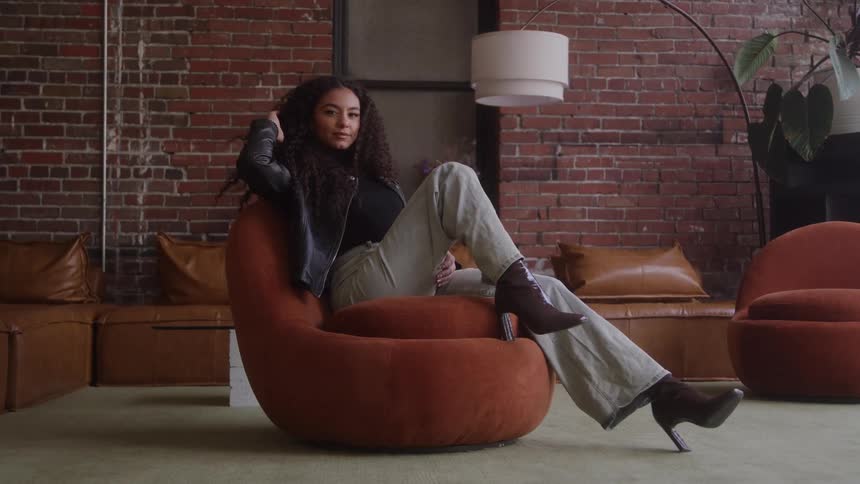 A woman sits confidently on a chair in a stylish modern loft
