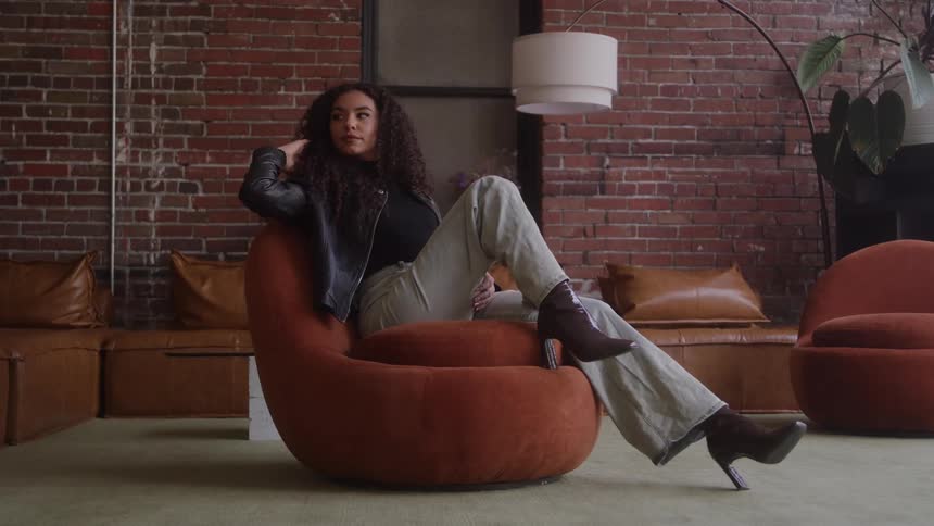 Biracial young woman sitting on a puffy chair modeling and playing with her hair indoors during day time