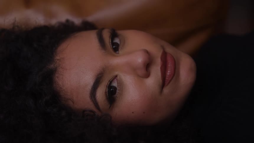 Woman lying sideways with direct gaze and neutral expression on cushioned surface