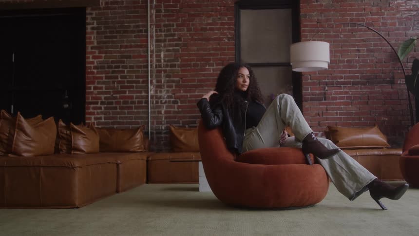 A woman sits confidently on a modern chair in a stylish loft