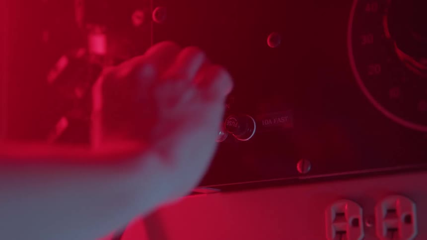 The video is a closeup of a persons hand illuminated by a deep red light flipping a toggle switch labeled power on an electronic devicethe surrounding panel is dark and industrial featuring what appears to be a large analog dial and two