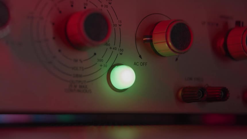 The provided video clip which appears to be a closeup of a piece of electronic or scientific equipment can be described in two lines as followsa persons hand turns a dial on an instrument panel and a small green indicator light immediately illumin