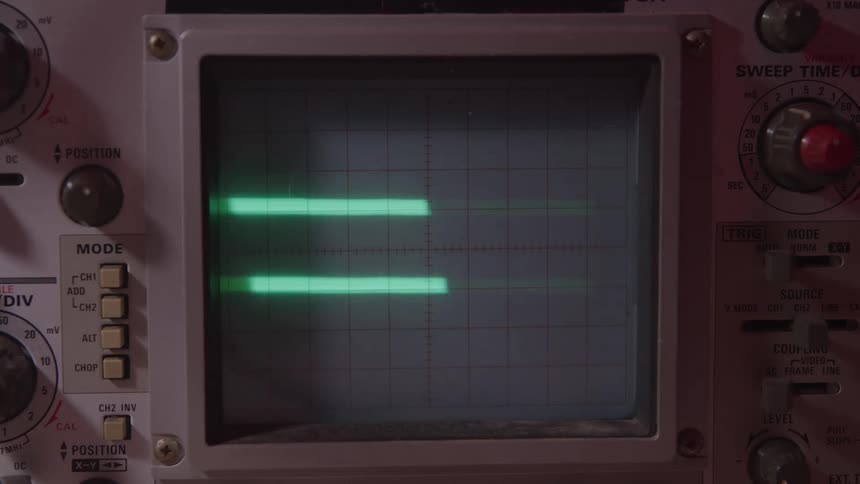 The video is a closeup shot of an oscilloscope screen displaying two parallel horizontal luminous green lines the screen has a grid pattern and the surrounding device shows various control knobs and buttons typical of vintage electronic testi