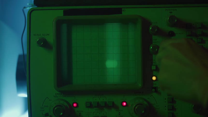 Hand adjusting the controls of an oscilloscope with a glowing green screen