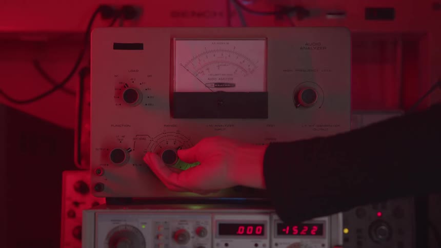 Hand adjusting frequency knob on vintage audio analyzer lit by red light