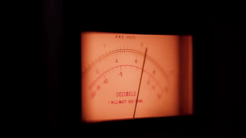 The video shows a closeup of an illuminated orangetinted analog volume or voltage meterthe needle on the meter is consistently moving and fluctuating indicating a changing audio signal or power level being monitored