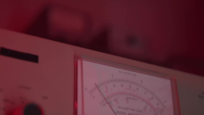 A voltohmmilliammeter device sits on a surface inside a room illuminated by red light