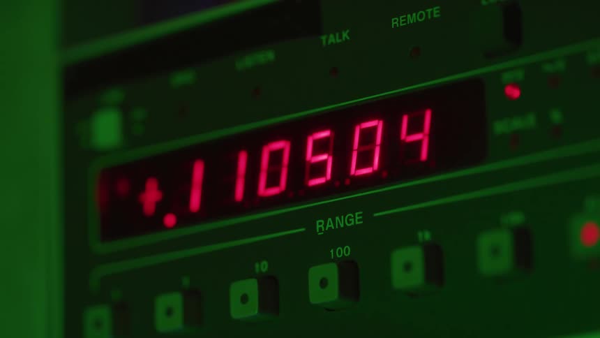 A dark electronic control panel displays glowing red numbers that change rapidly green light illuminates the display and surrounding panel and text labels indicate the function of the equipment