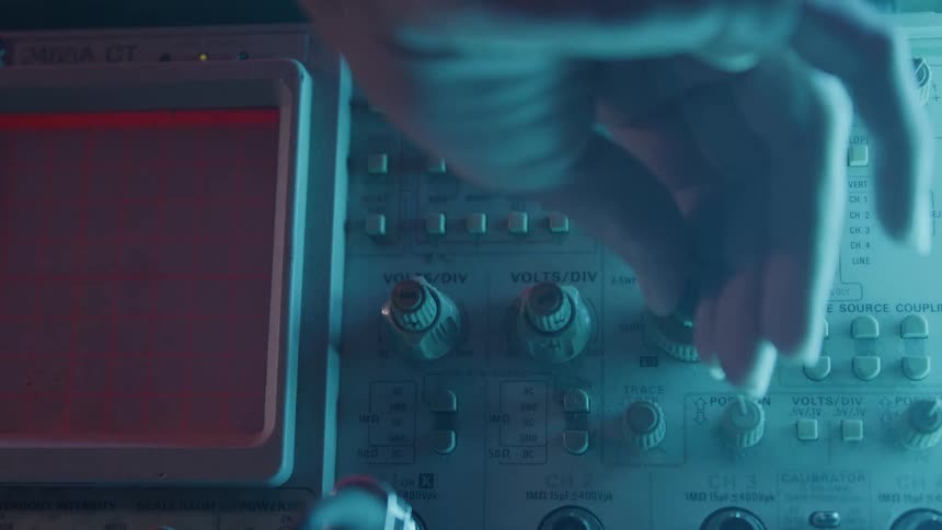 A persons arm operates an oscilloscope machine adjusting the knob