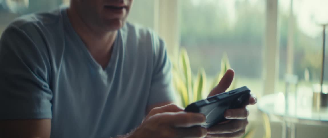 A man plays a mobile game on his smartphone in a softly lit room