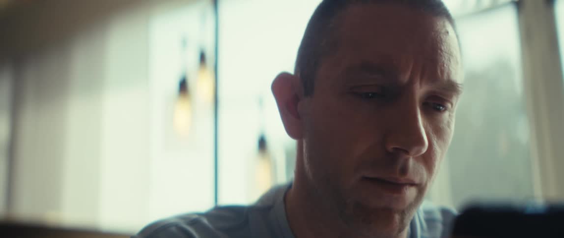 Person in light shirt holds device with both hands in front of hanging lights and blurred window