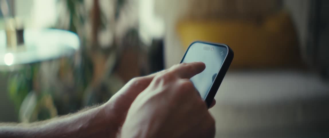 A person sits indoors scrolling through their smartphone at midday