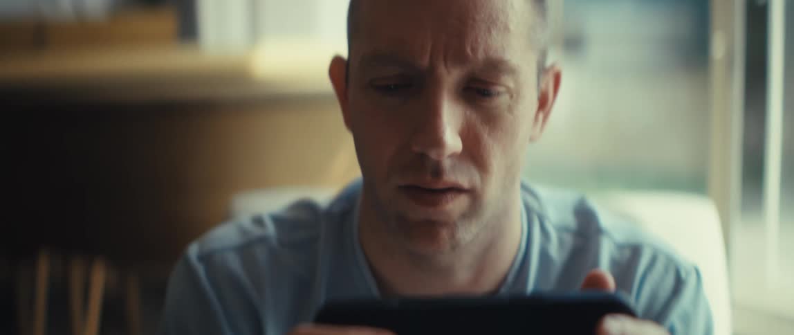 A man sitting in a caf holding a cellphone with both hands and looking at it