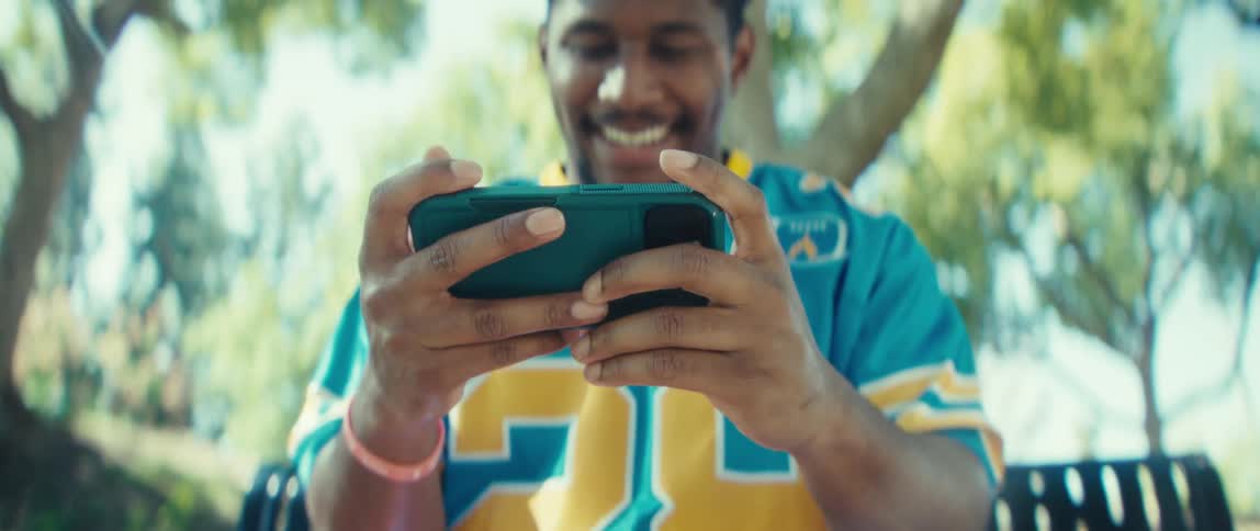 Man smiles while holding his phone in a sunlit park