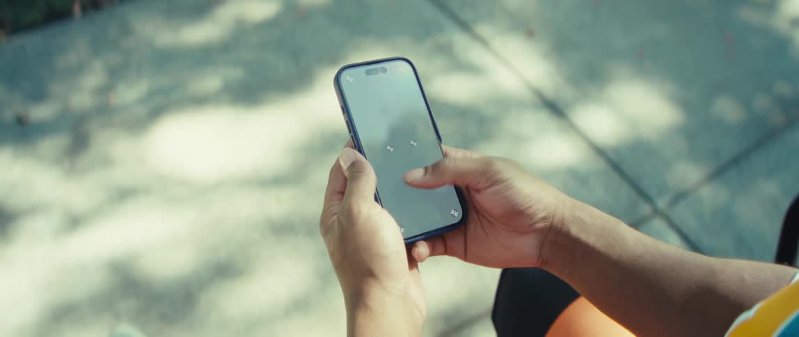 Person holds a smartphone while typing outdoors