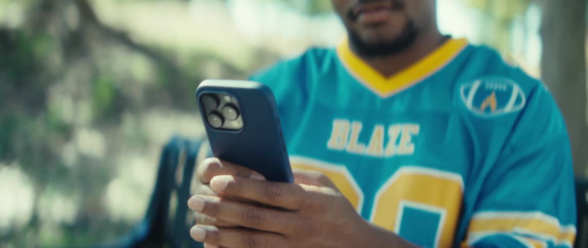 Man holds a smartphone while wearing a sports jersey labeled blaze