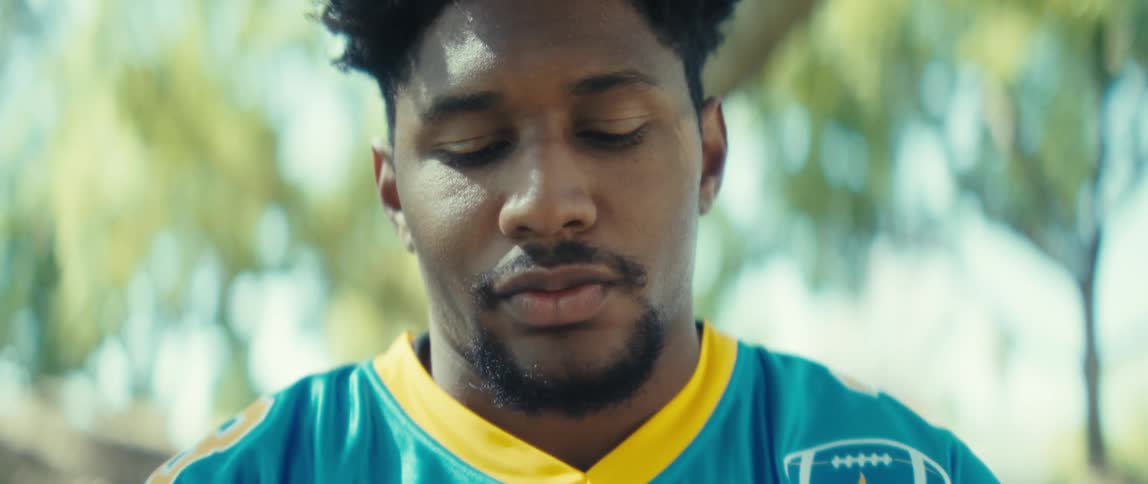Man in a blue sports jersey looks at his phone outdoors