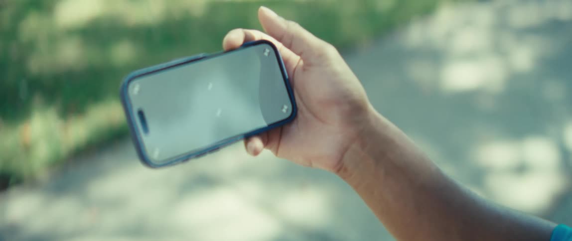 A man watching the screen of a smartphone while standing outdoor at midday
