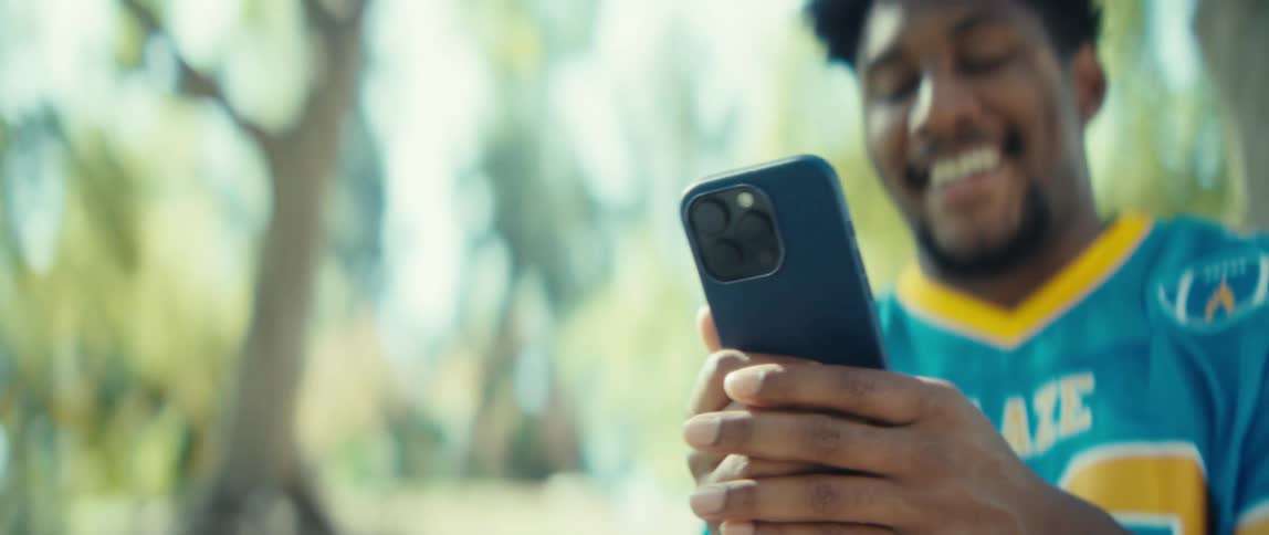 Man smiles while scrolling on a smartphone outdoors during the daytime