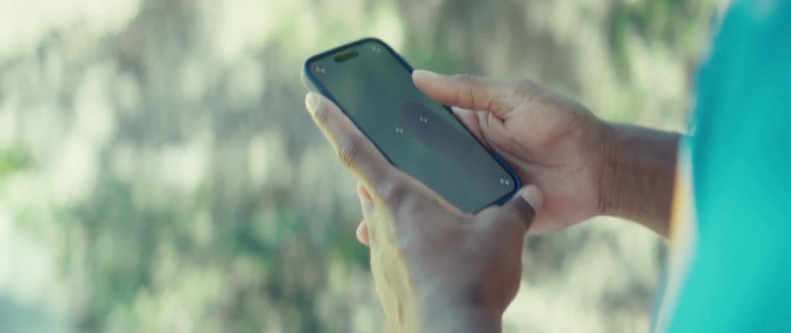 Fingers interact with phone screen in outdoor setting with blurred vegetation background