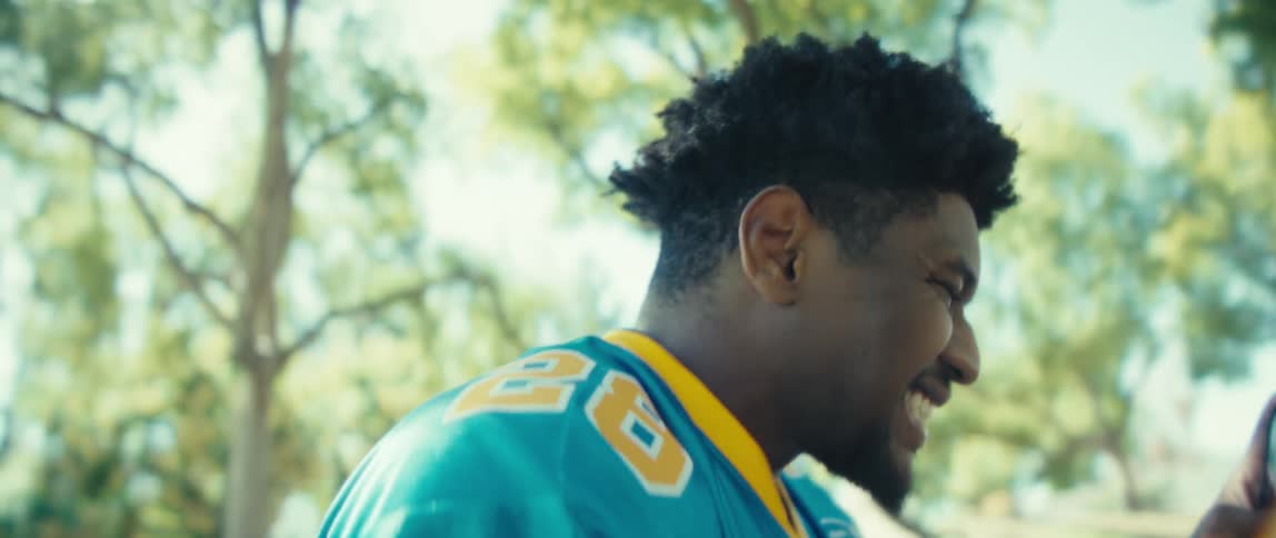 The video features a man wearing a blue and yellow jersey with the number 26 who is laughing and celebrating enthusiasticallyhe is holding a smartphone and initially pumps his fist and points before looking down at the device suggesting hes r