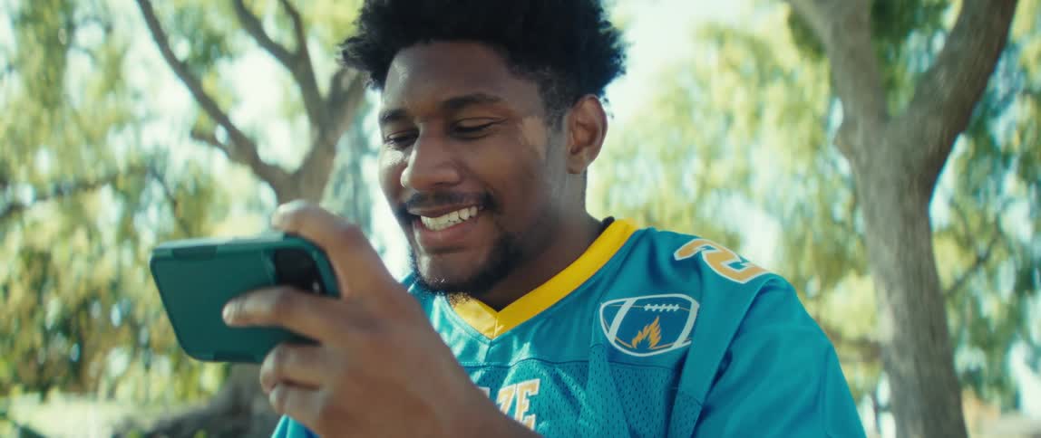 Man smiles while holding his phone in a sunlit park