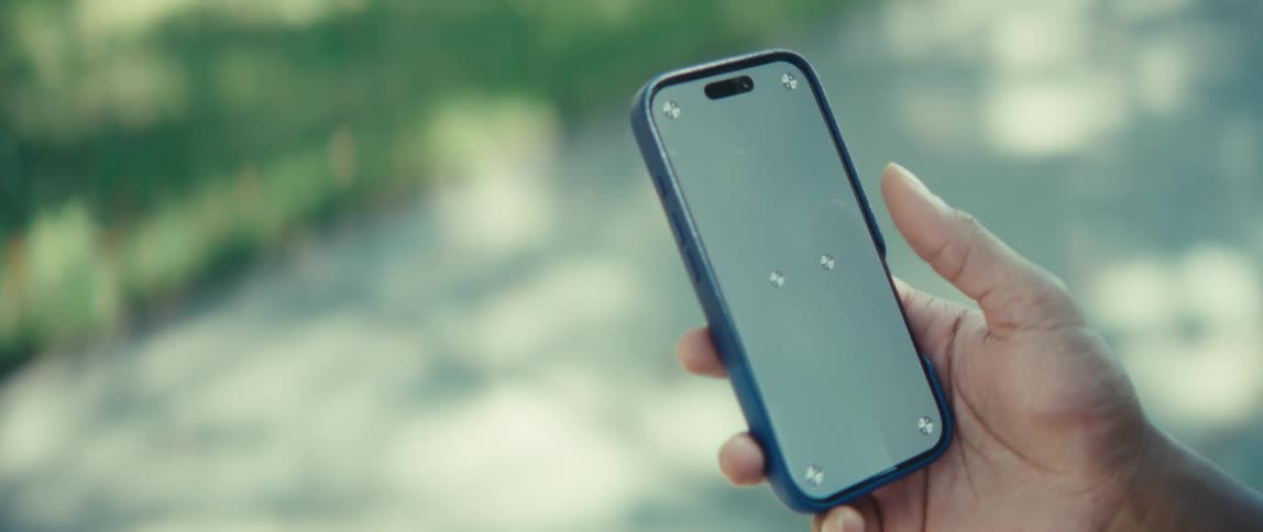 A man outdoors holding a cellphone and sliding his finger across the screen