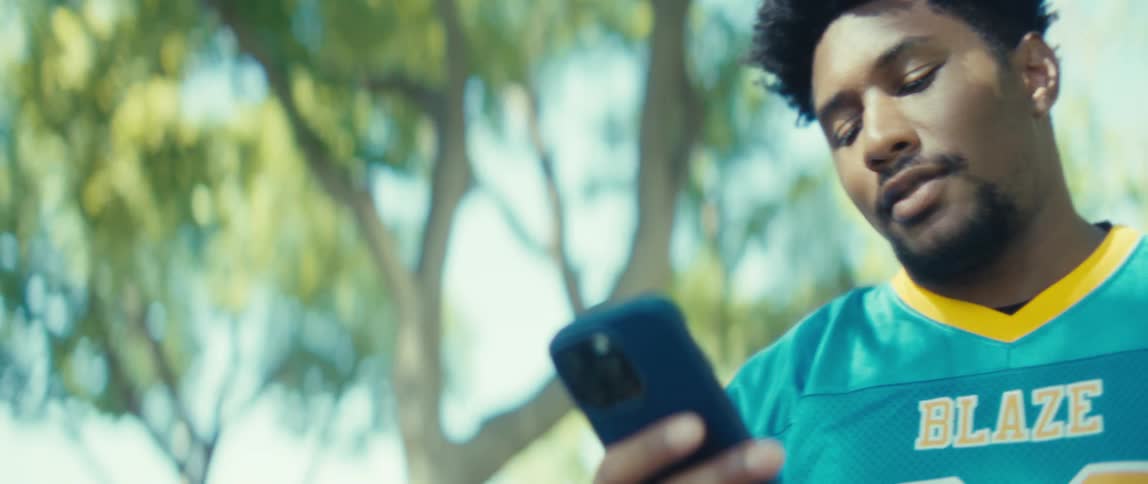 A man is looking at his cellphone as he walks through trees
