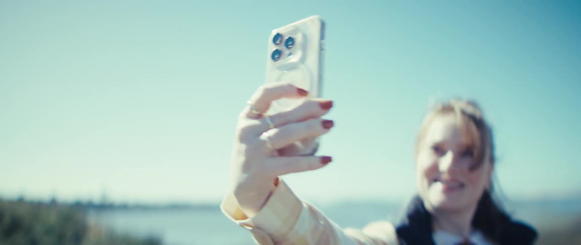 Woman holds a clear smartphone while smiling under the sunny sky