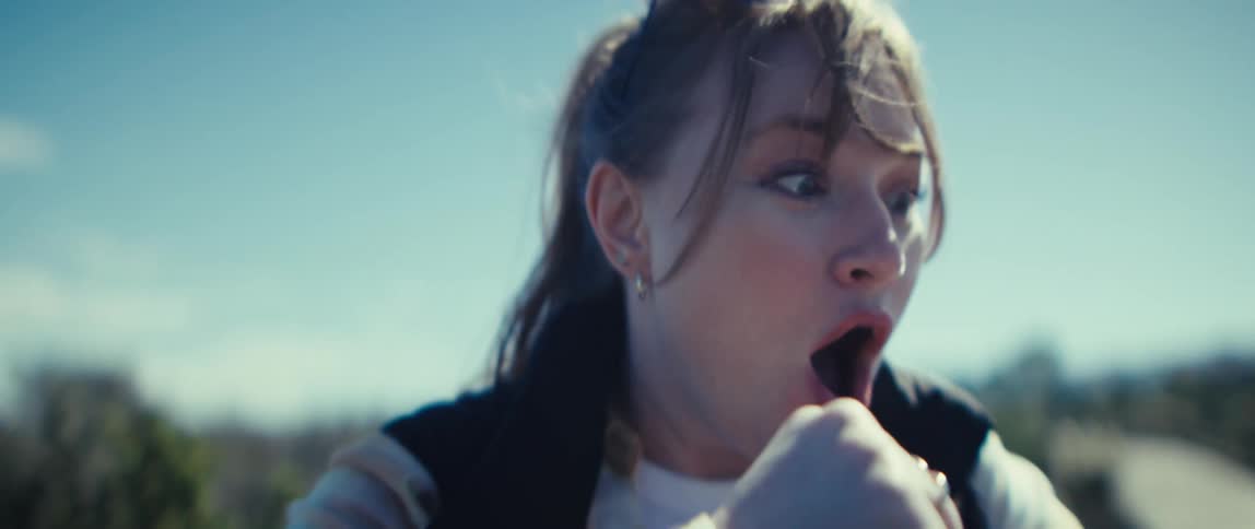 A young woman hiking in the woods wearing a jacket suddenly becomes excited as she watches content on her mobile device under the sun