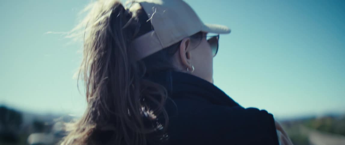 A young woman wearing sun hat and glasses and a jacket walking outdoor on a path in the wild midday