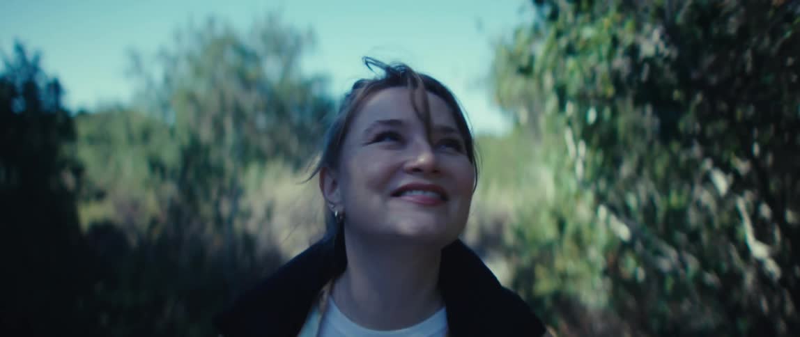 A young woman walks along a path in the woods on a sunny day spinning and smiling with joy