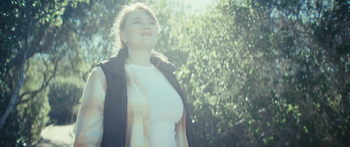 A woman walks down a path through a forest on a sunny day