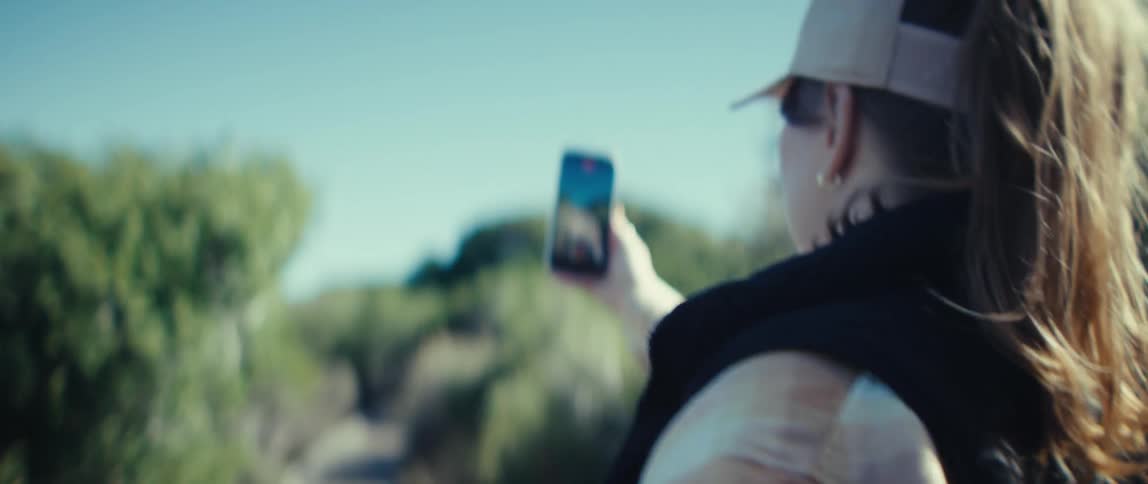 A woman is filming with her cellphone as she hikes through a forest