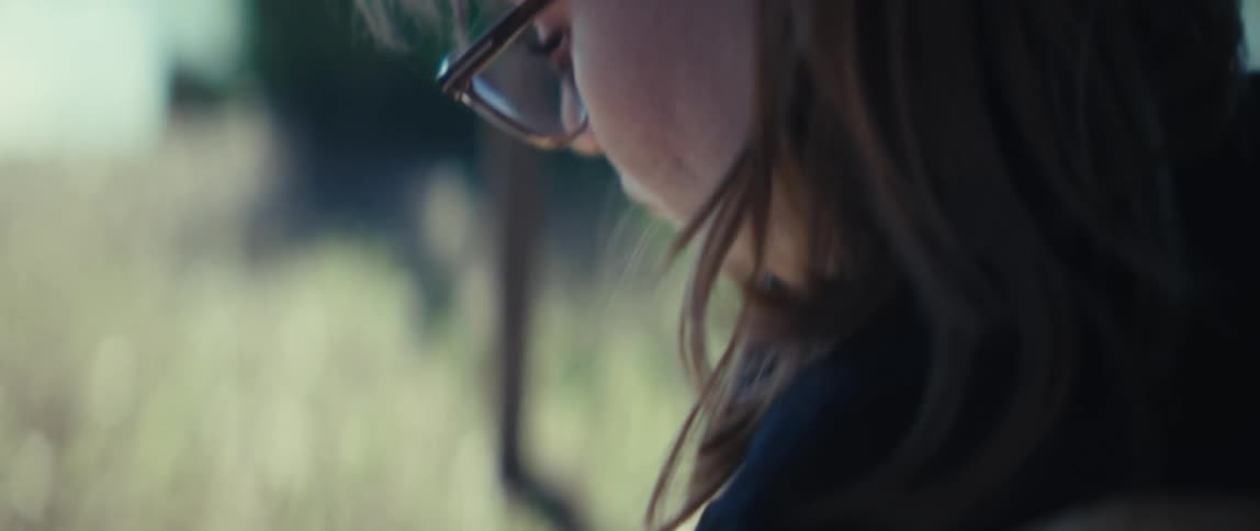The video opens with a closeup of a persons hands as they write on a small pad of paper with a pen with their fingernails painted redit then cuts to a tighter shot of the persons face revealing they are wearing glasses and focusing intentl