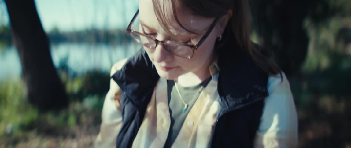 The video starts with a person seated outdoors working with a watercolor palette and a small green notebook using a water brush penthe shot then focuses on the persons face showing them wearing brownframed glasses and concentrating intent