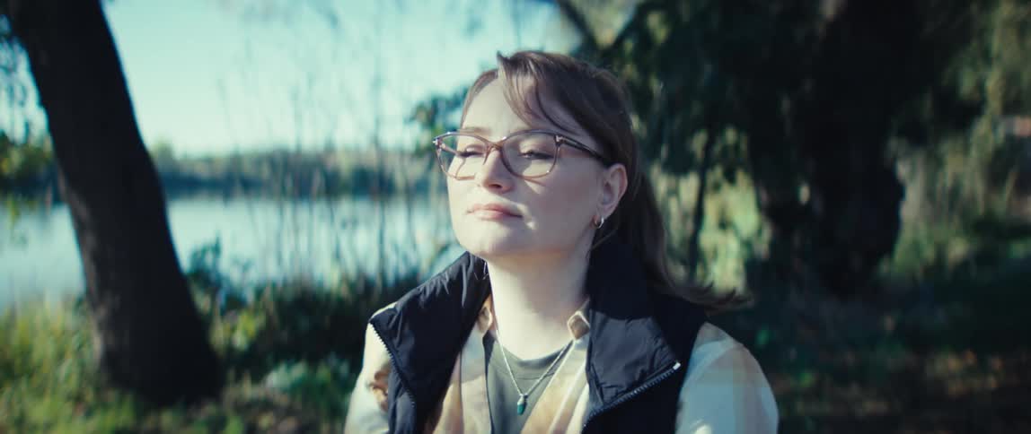 A woman is sitting on the grass at the edge of a lake