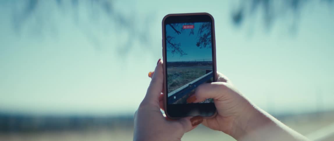 Hands hold a phone recording a video of a landscape under a blue sky
