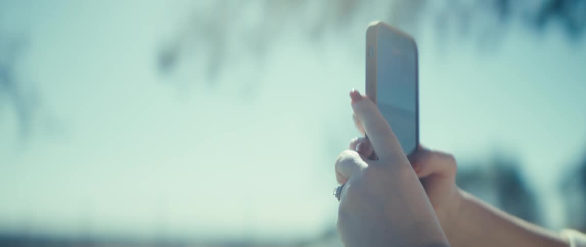 The video begins with a closeup of a persons hands holding a smartphone vertically appearing to be recording video of a scenic outdoor landscapethe shot then pans to the persons face revealing a woman wearing glasses and smiling as sh