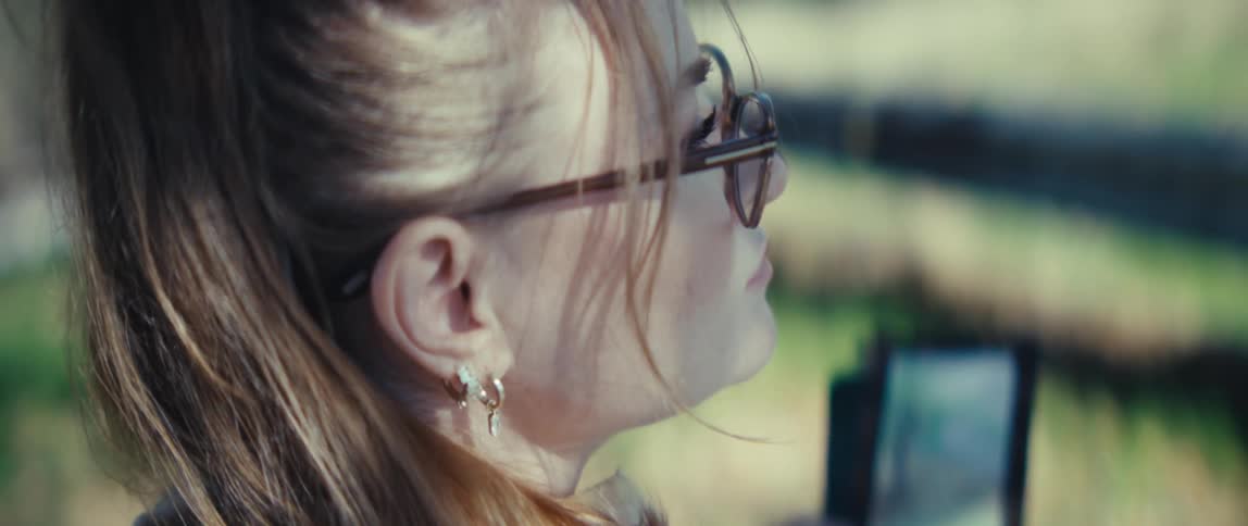 A woman looks around outside then marks her phone with a stylus