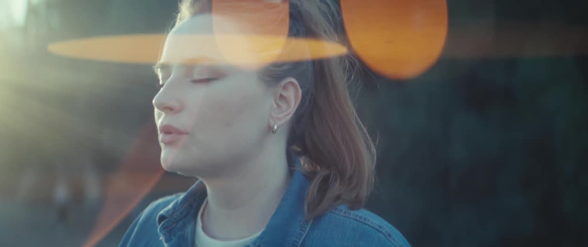Woman with closed eyes under sunlight wearing a denim jacket