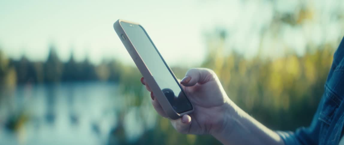 Hand holds a smartphone while a finger touches the screen near a lake