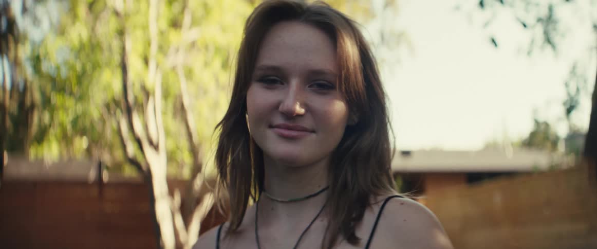 A young woman with long brown hair smiles while outdoors in the woods