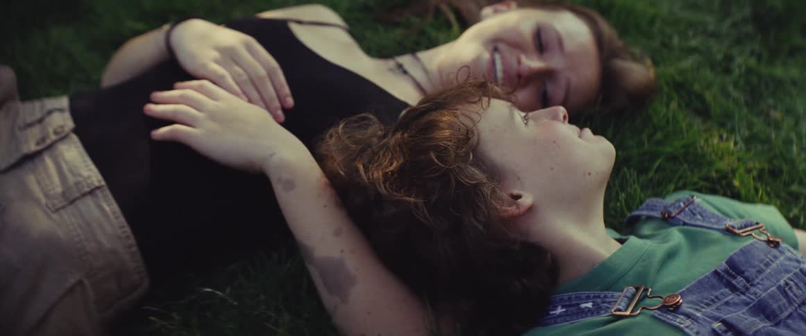 Two friends lie on the grass laughing together under the warm sunlight